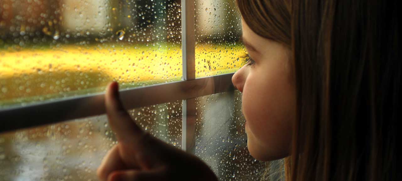 Bambina osserva le gocce di pioggia alla finestra