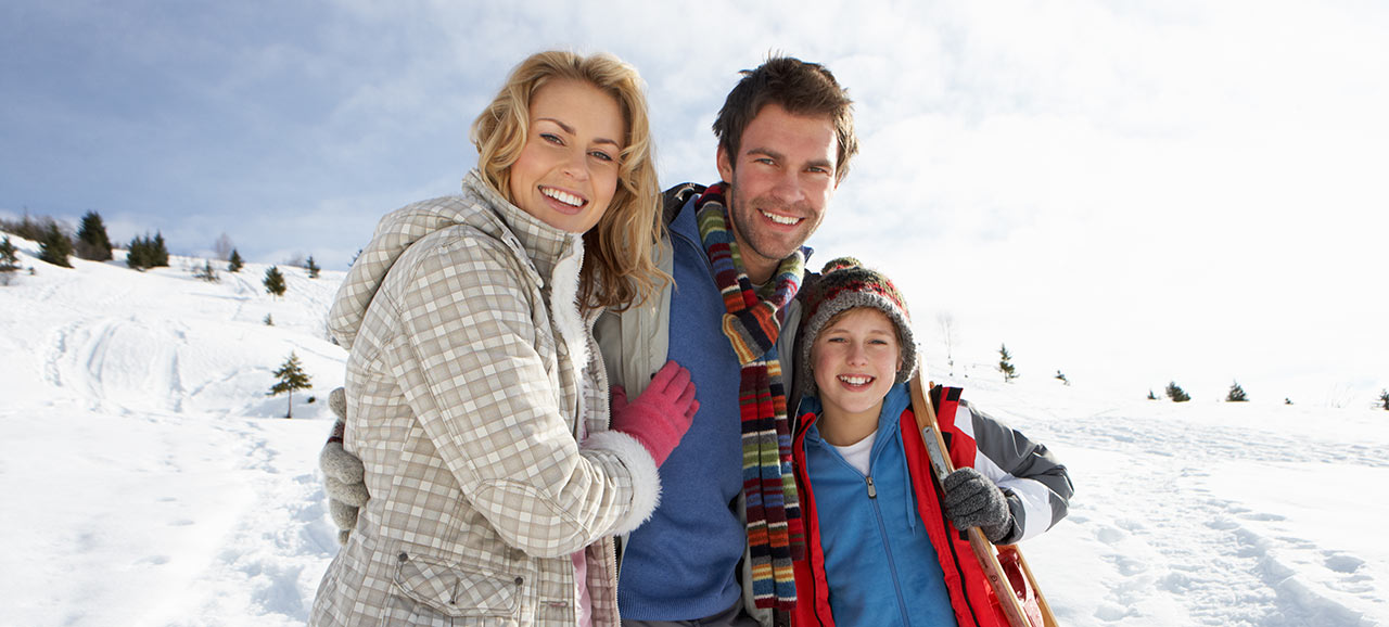 Eine lächelnde Familie mit Mutter, Vater und Sohn auf einem Gruppenfoto mitten in einer schneebedeckten Landschaft