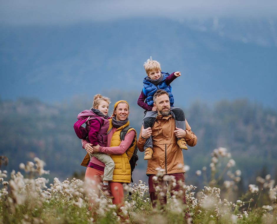 Happy parents with their young children riding on their shoulders during an autumn walk amid colorful nature. Healthy lifestyle concept. Carrying kids on shoulders during the hike.