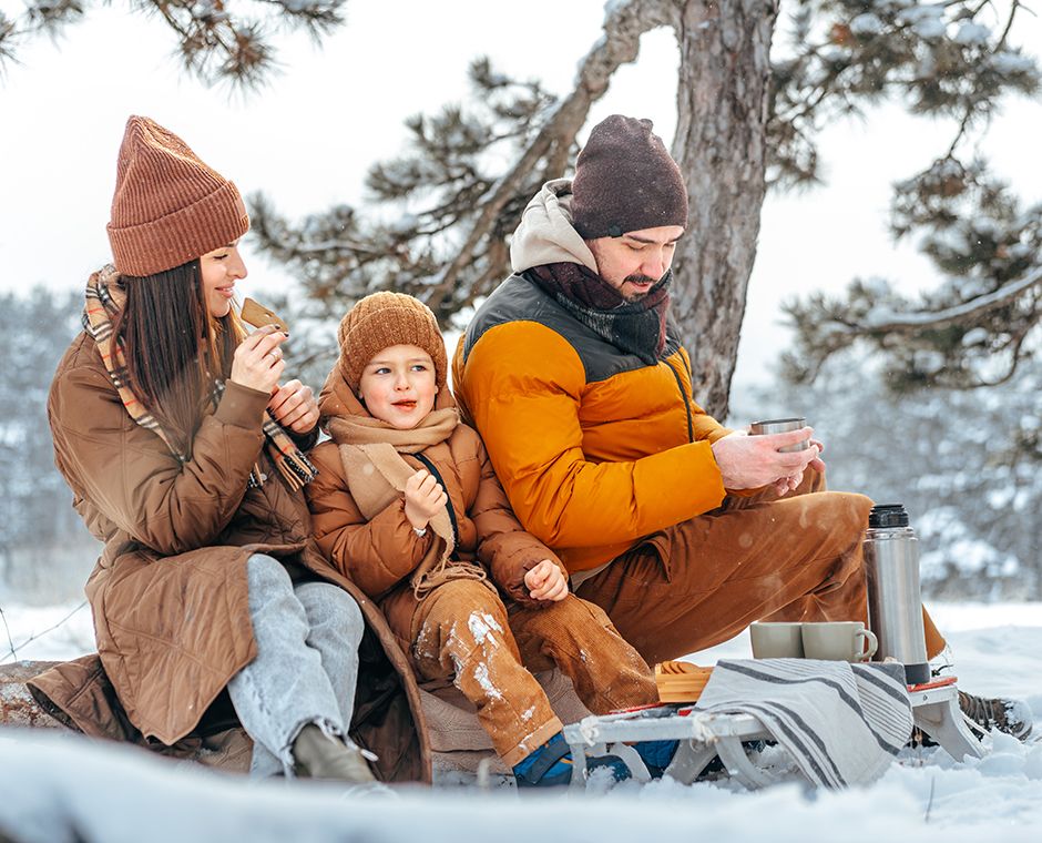 Happy family with mugs of hot tea spending time together in a winter forest, close-up