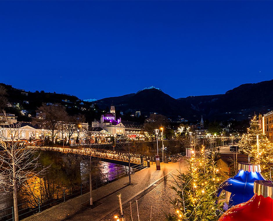 Romantic Christmas Market in Merano along the Passer River, illuminated stalls and light reflections on the water