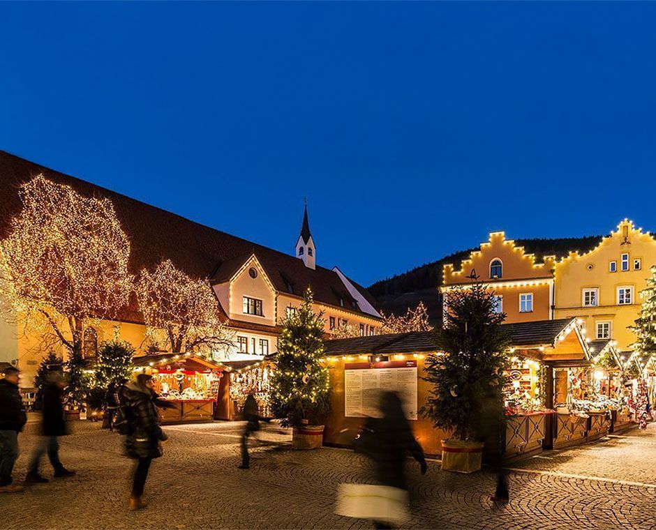 Christmas Market in Vipiteno with the Tower of the Twelve in the background, illuminated stalls and an evening atmosphere