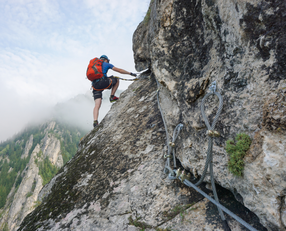 Una foto mozzafiato di un giovane che si arrampica su una scogliera in una giornata fredda e nebbiosa.