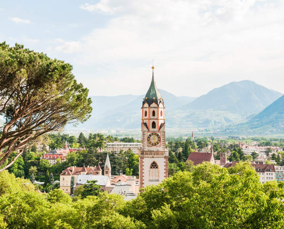 Panorama su Merano con la torre della Chiesa di San Nicolò, circondata da parchi e montagne.