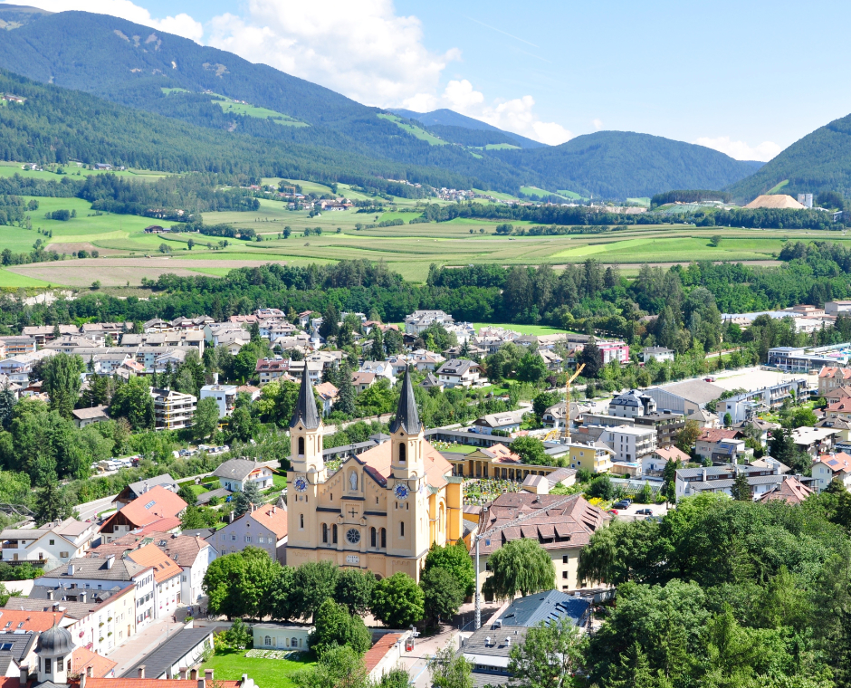     Veduta panoramica di Brunico con la chiesa parrocchiale e la valle verde circostante.