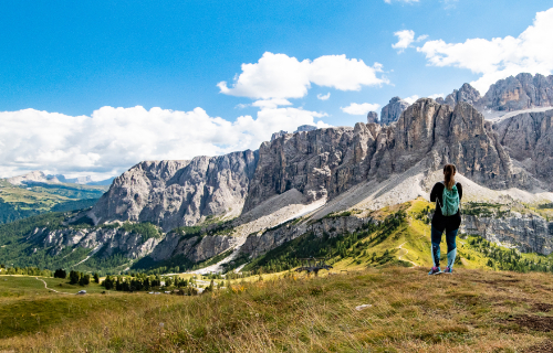 Hikers with backpacks in front of a panoramic view of the Dolomites massif under a cloudy sky.