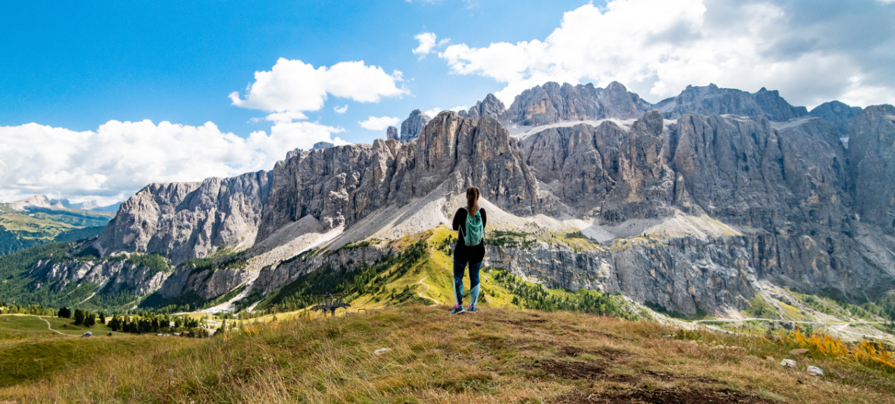 Escursionista con zaino davanti al panoramico massiccio dolomitico sotto un cielo nuvoloso.