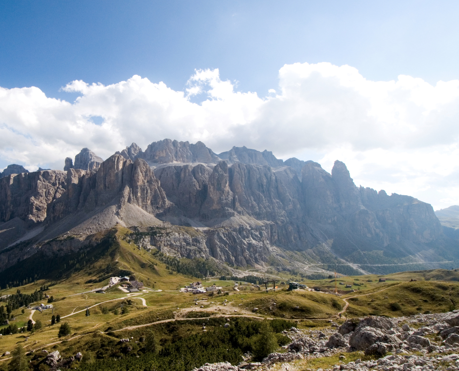 Panorama sulle Dolomiti con prati alpini, sentieri e rifugi ai piedi delle montagne.