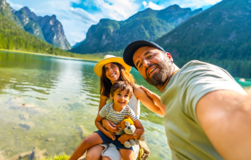 Happy family takes a selfie at the mountain lake with baby in arms and stuffed animal