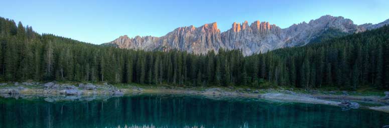 Il lago di Carezza circondato da alberi e montagne sullo sfondo