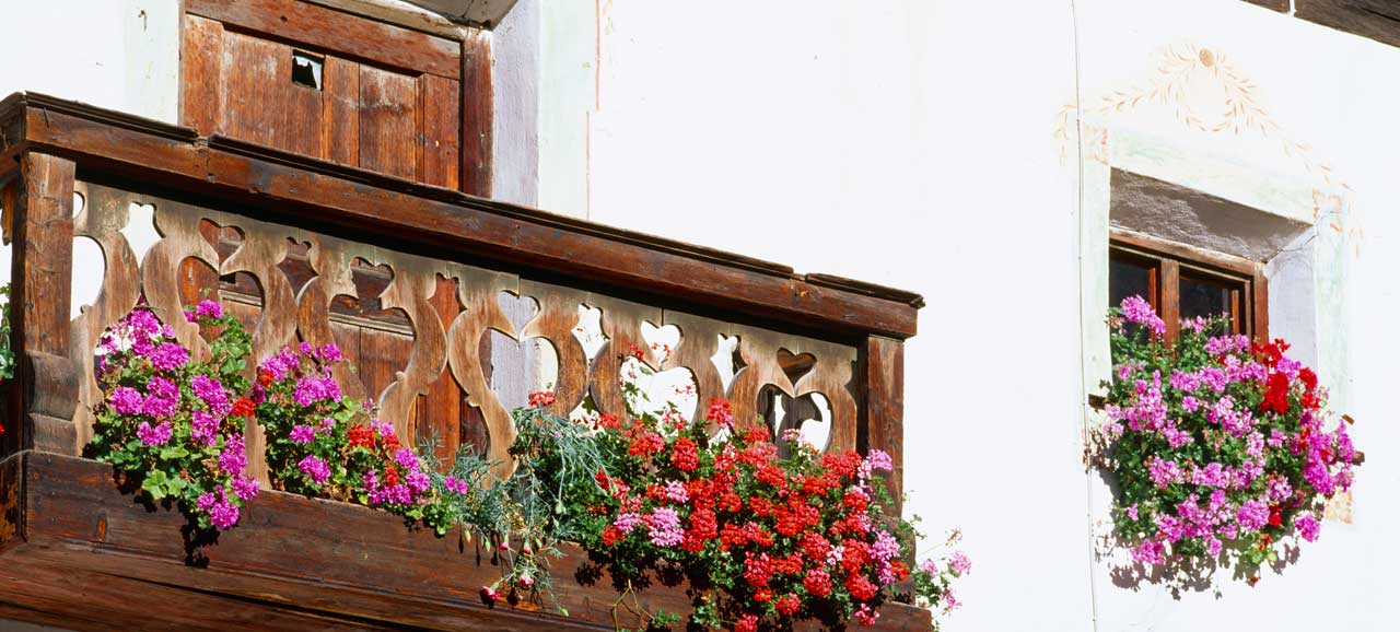 Holzbalkon in Südtirol mit bunten Geranien