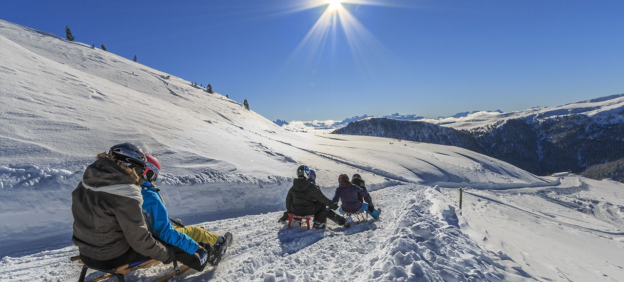 Rodler auf der Rodelbahn in Reinswald (Sarntal) im Winter mit verschneiten Bergen im Hintergrund und bei strahlendem Sonnenschein