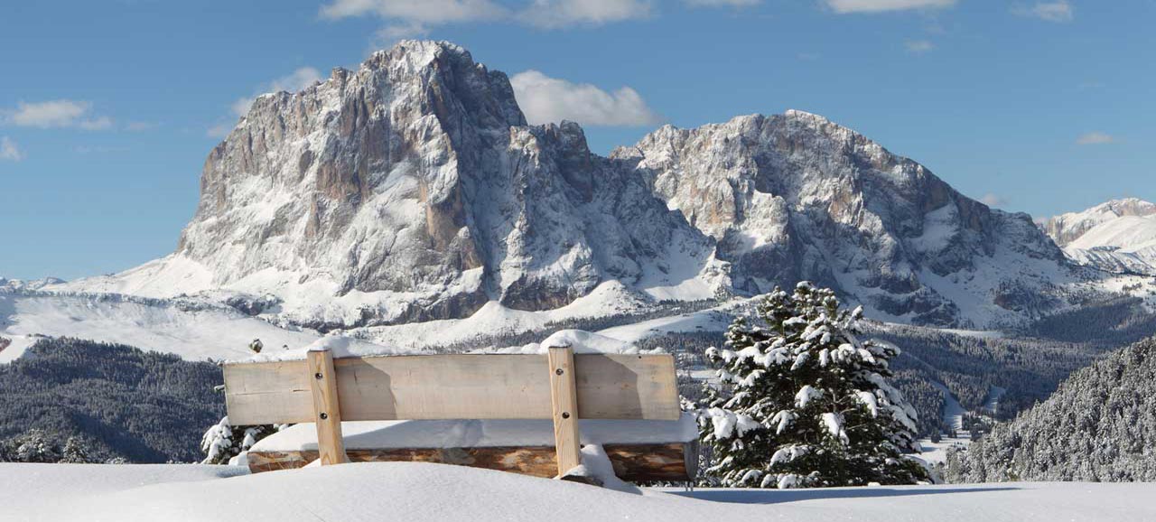 Snow covered bench in front of the Sassolungo