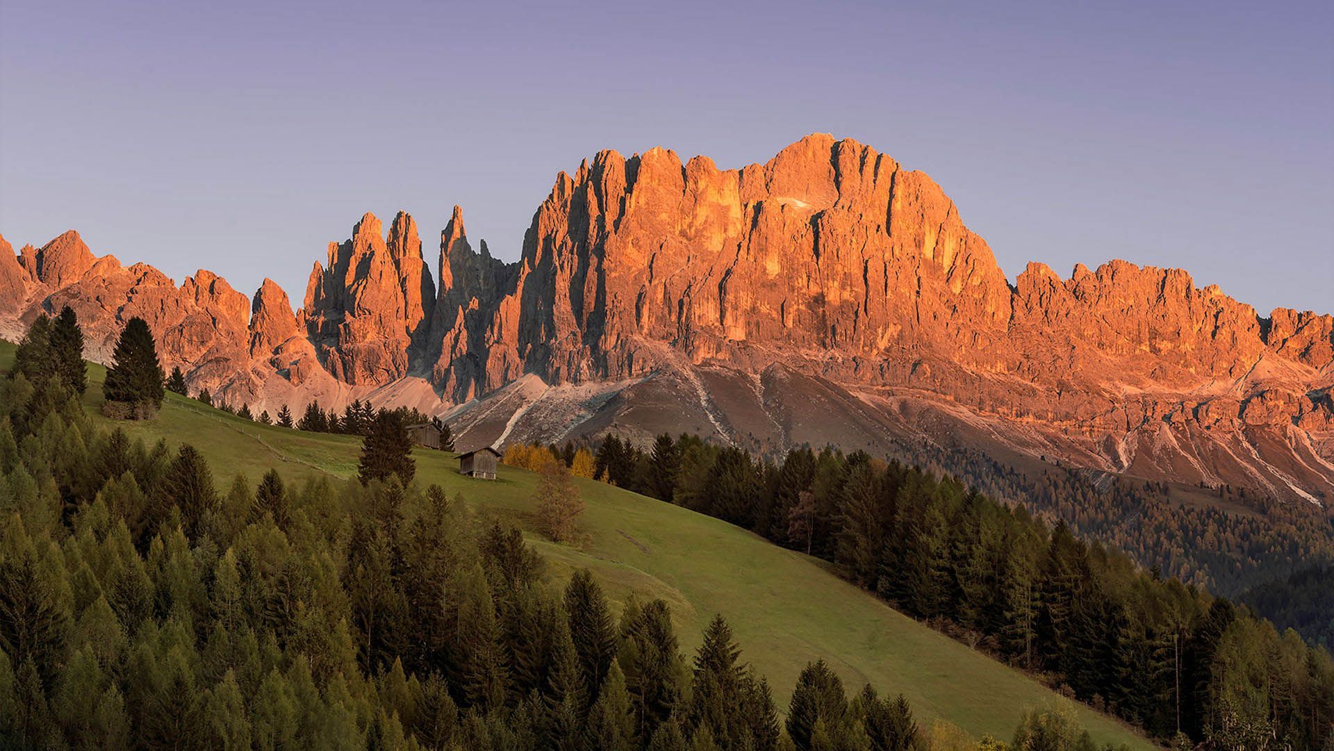 The Catinaccio glows pink at sunset above South Tyrolean forests and mountain huts