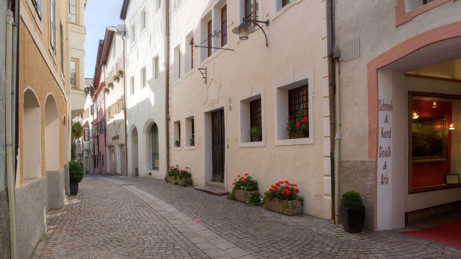 Historisches Gässchen im Zentrum von Klausen mit bunten Häusern, kunstvollen Schildern und Blumen an den Balkonen