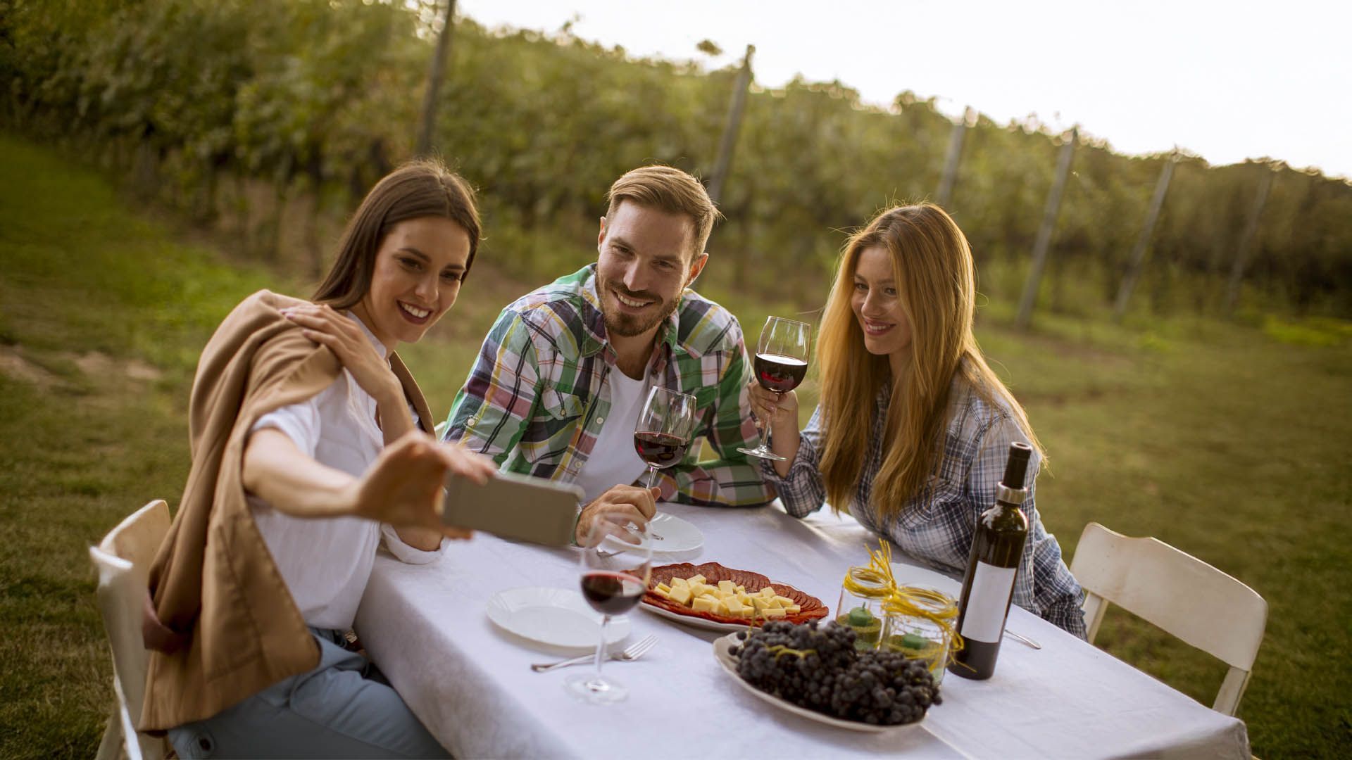 Three friends toast and take a selfie among the vineyards.