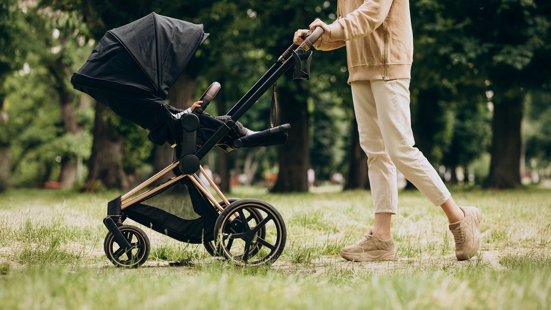 A parent pushes a pram along a path in the countryside.
