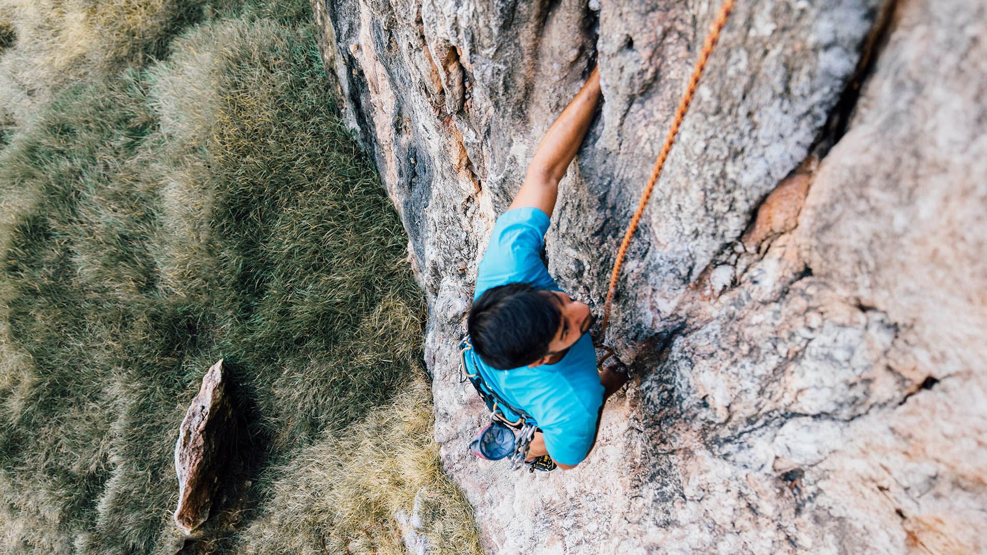 Climber with rope and harness ascends an outdoor rock wall