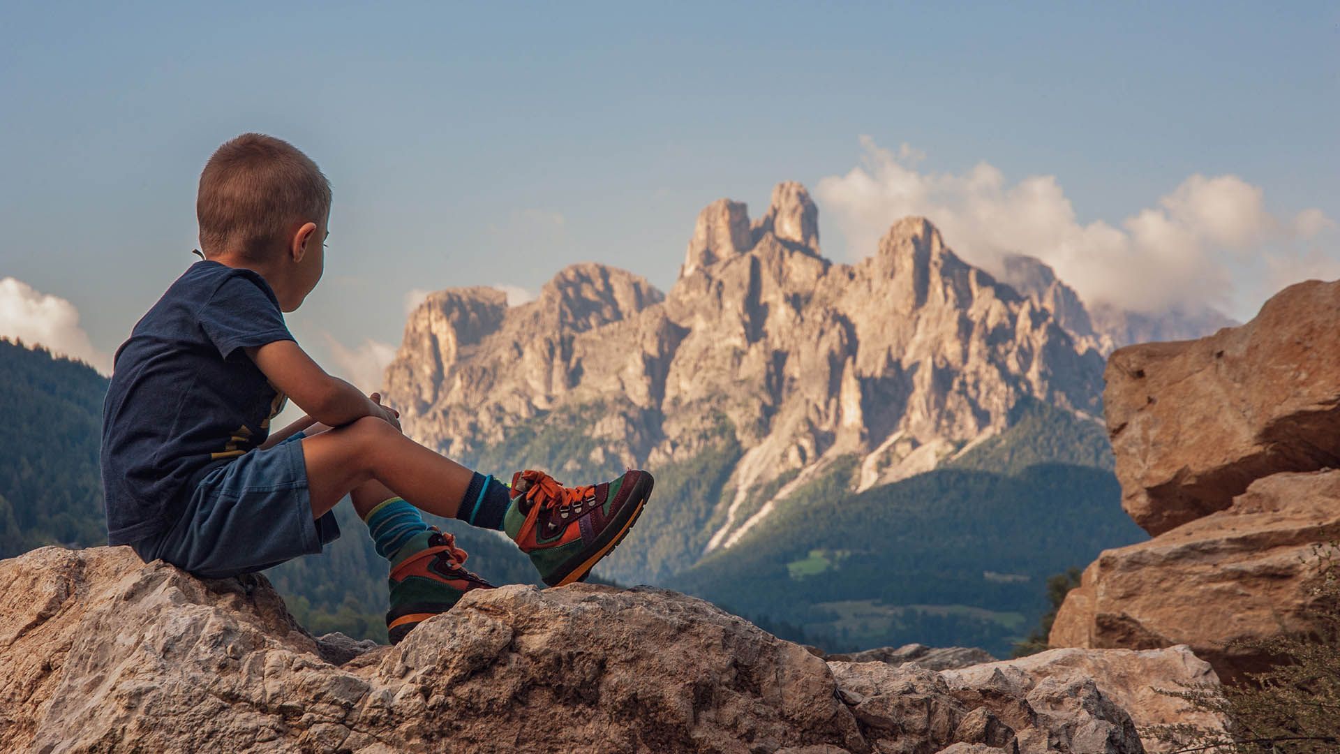 A child sits on a rock and observes the mountains during a hike.