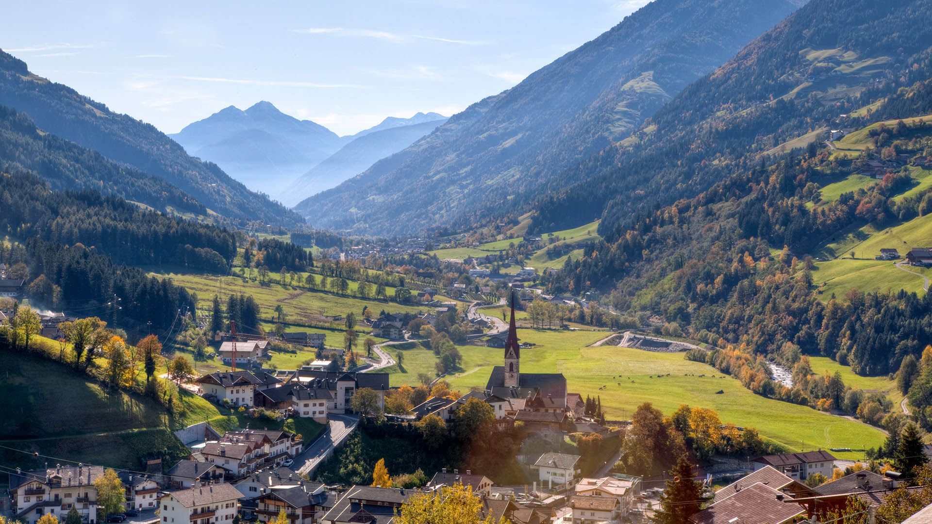 Vista su San Leonardo in Passiria con chiesa, prati verdi e montagne che incorniciano la valle
