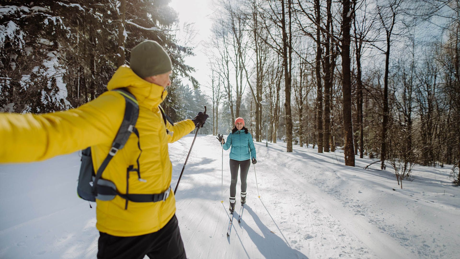 Coppia che pratica sci di fondo su un sentiero innevato tra gli alberi.