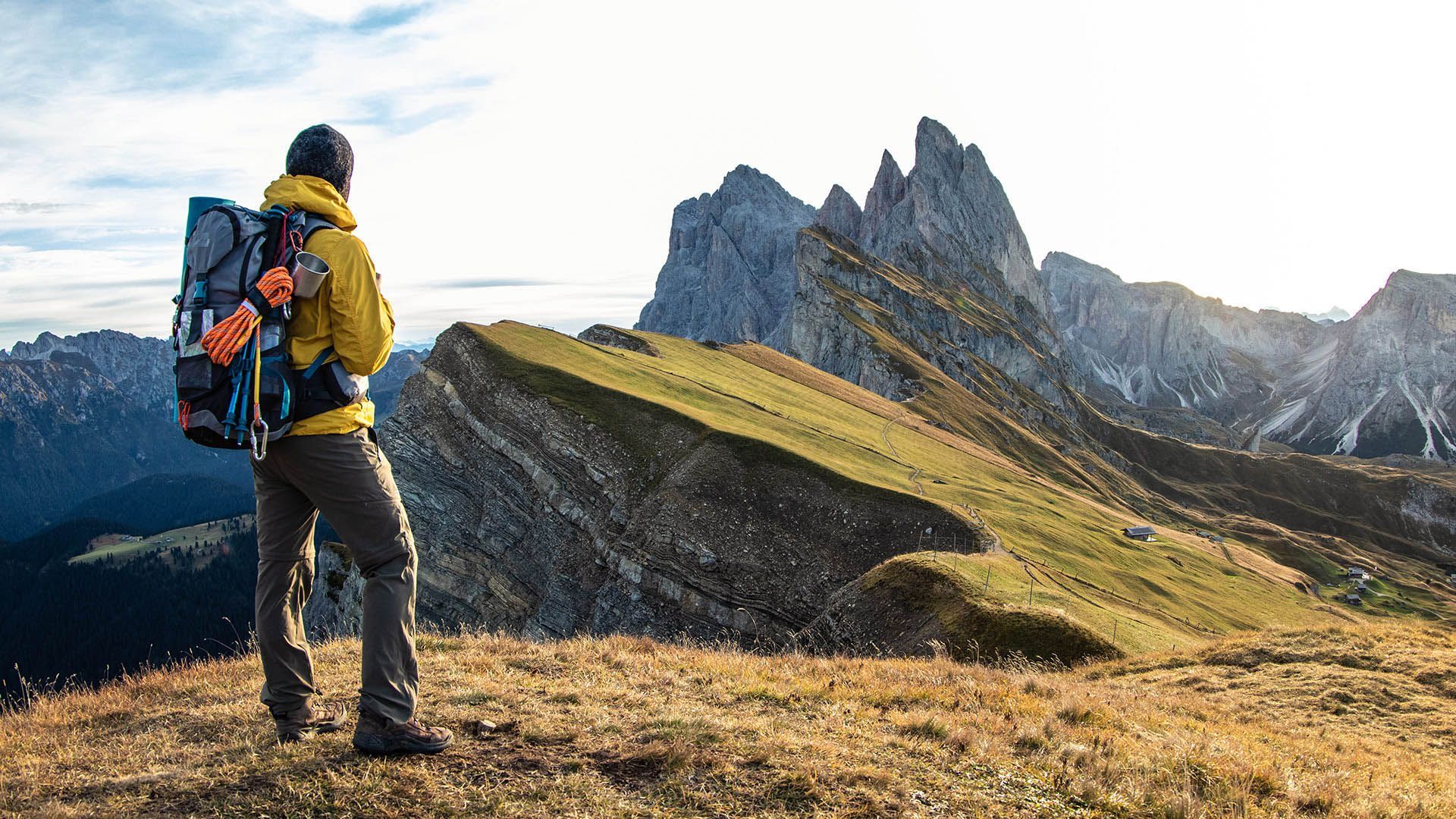 A hiker on a rocky outcrop observes an alpine lake surrounded by mountains.
