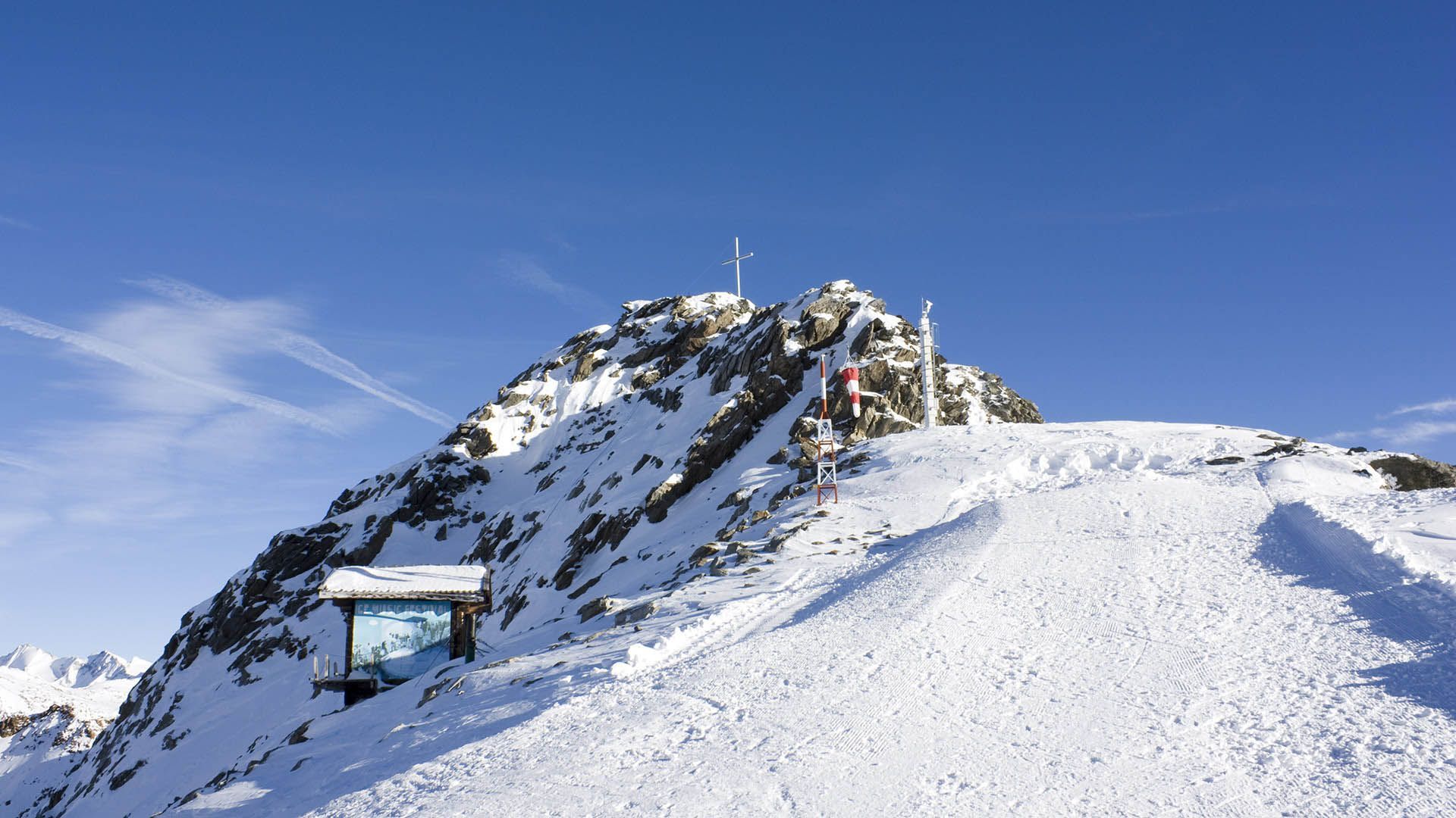 Snow-covered peak in Val Senales with cross, anemometer and blue winter sky