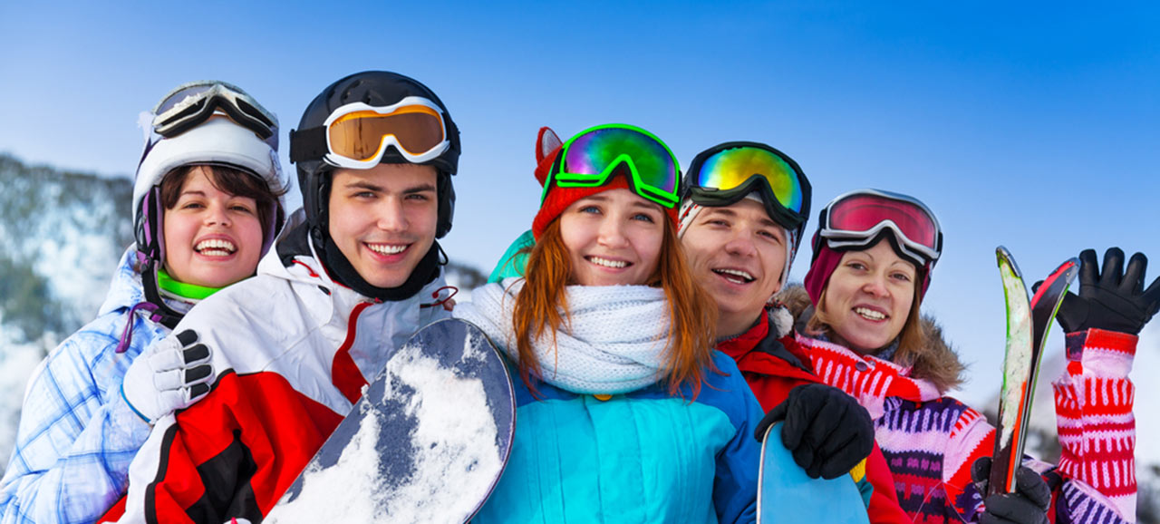 Foto di gruppo di cinque amici con snowboard e sci sulla pista