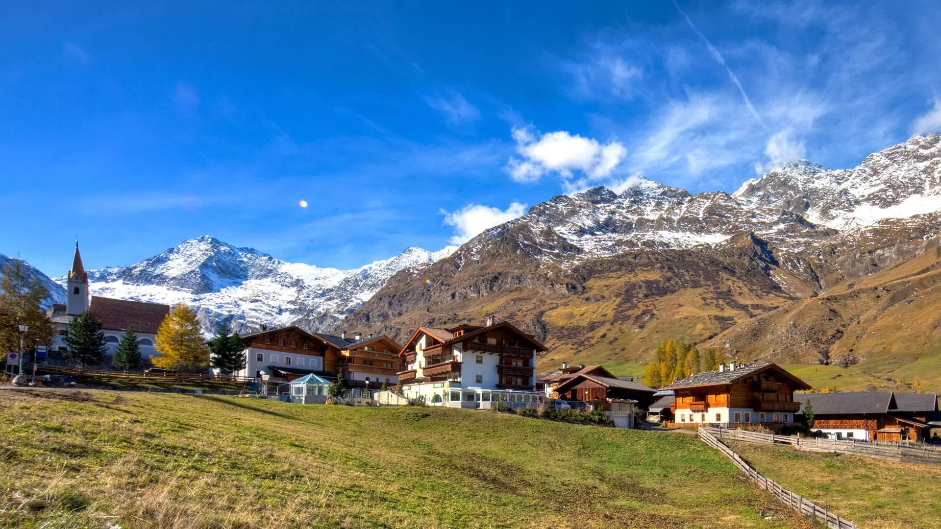 Chiesa e case a Plan in Val Passiria con montagne innevate e cielo azzurro in autunno
